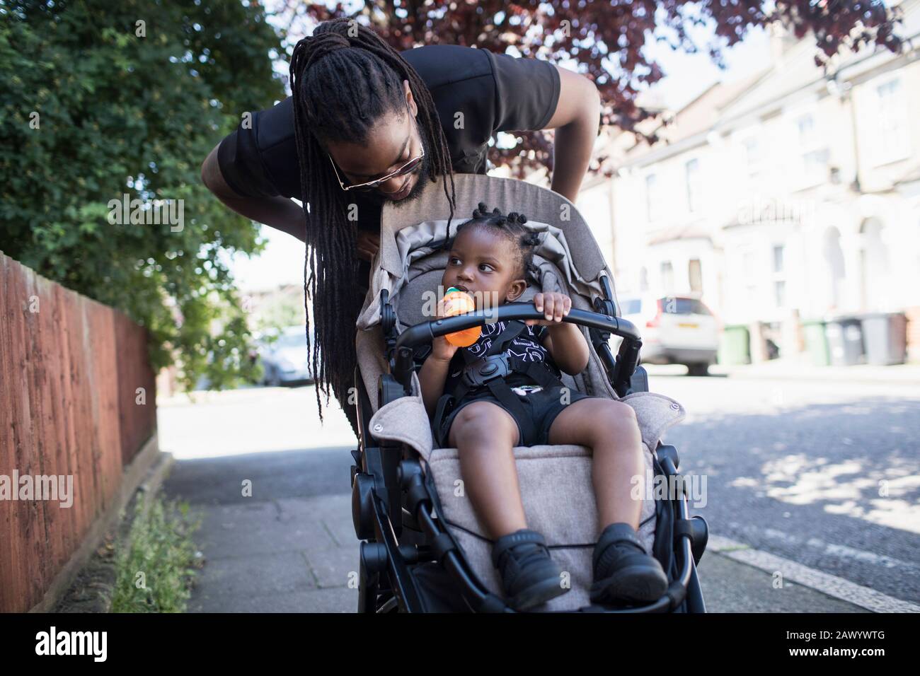 Father pushing toddler son in stroller on urban sidewalk Stock Photo
