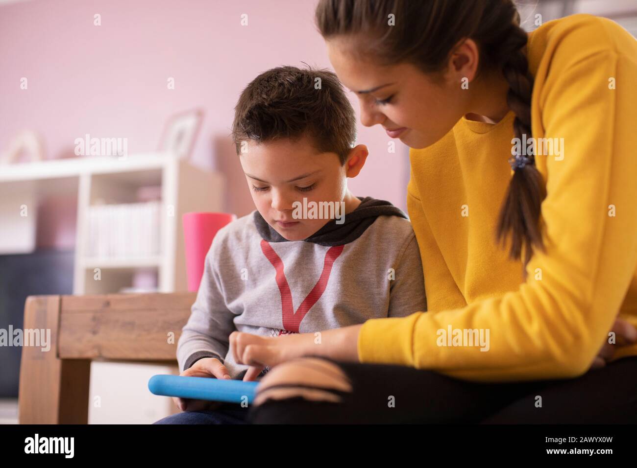 Sister helping brother with Down Syndrome using digital tablet Stock Photo