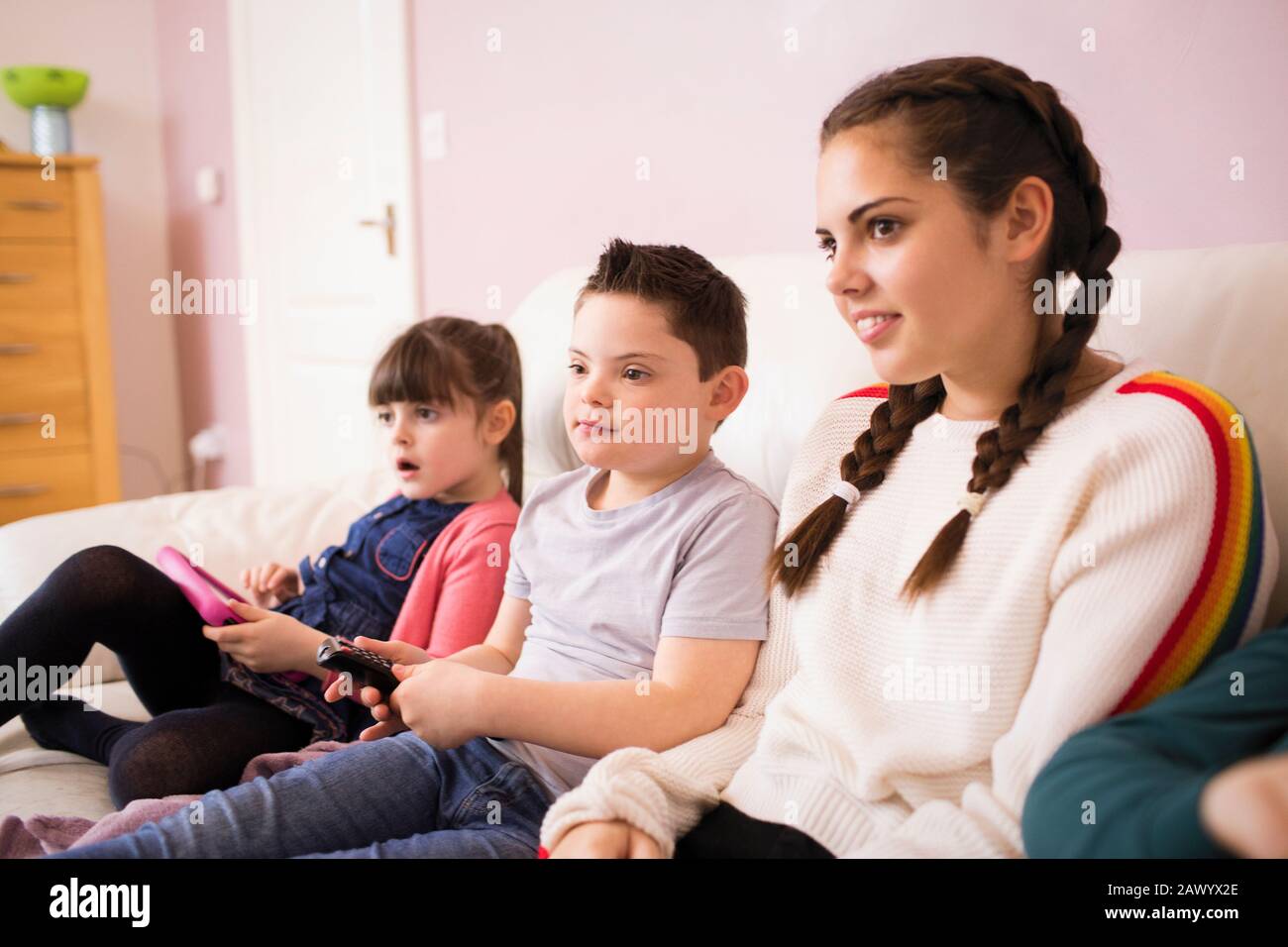 Boy with Down Syndrome watching TV on sofa with sisters Stock Photo