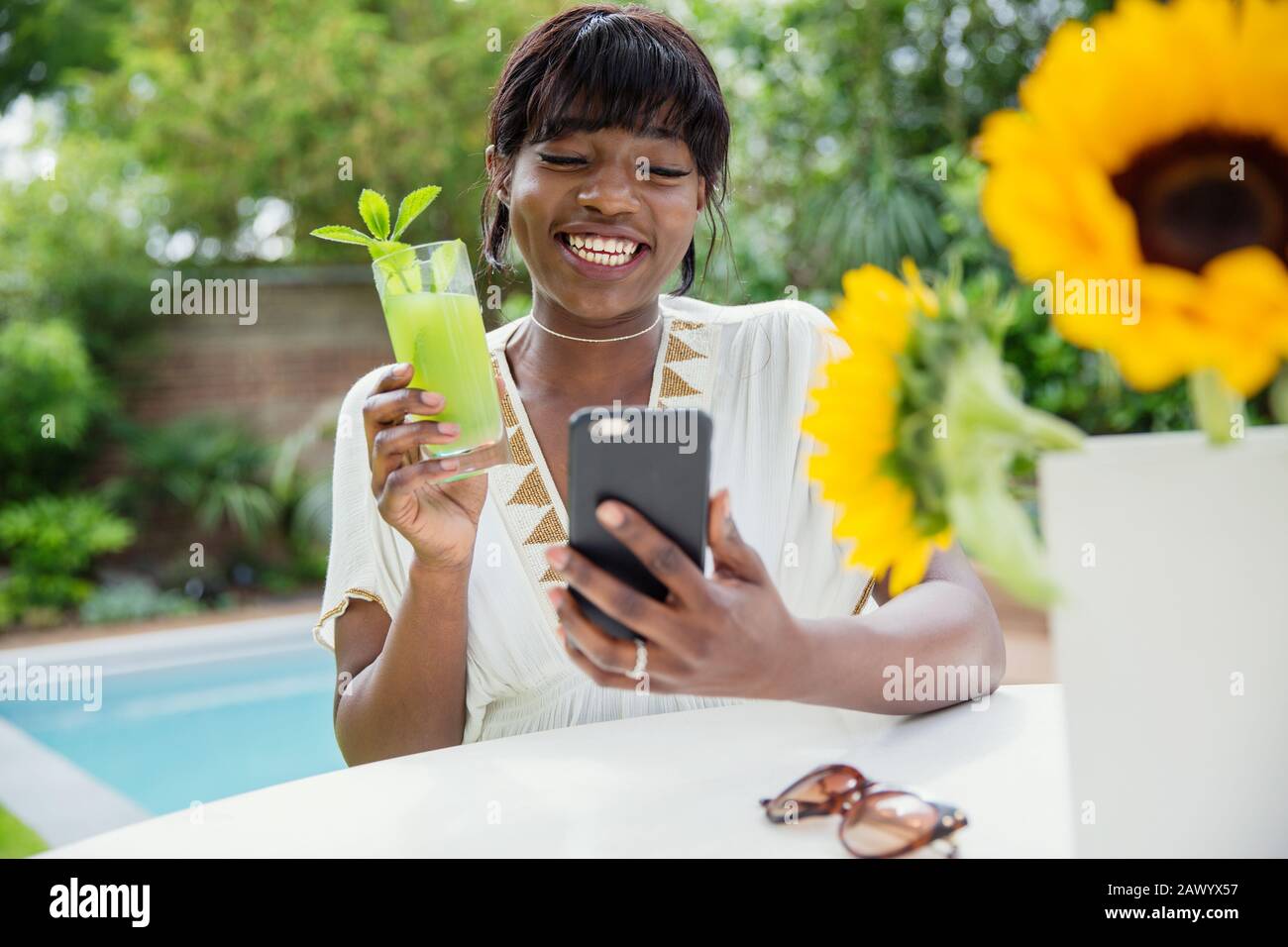 Happy young woman drinking cocktail and video chatting at poolside Stock Photo