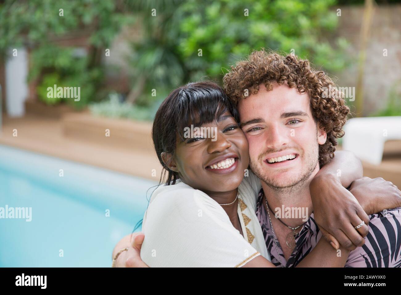 Portrait happy young multiethnic couple hugging at poolside Stock Photo
