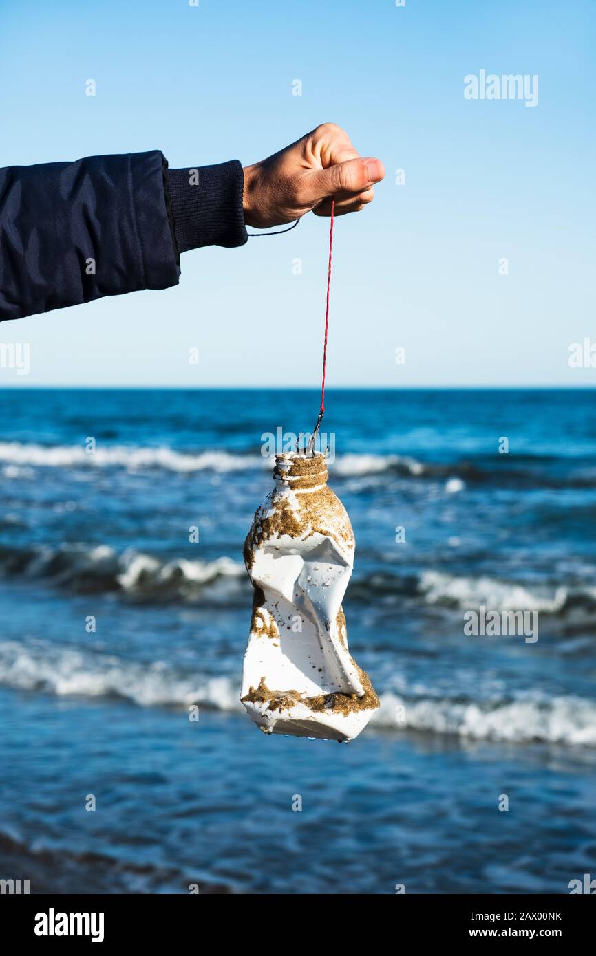 closeup of a man holding a fishing line with a used plastic bottle in the fish hook, freshly fished in the ocean, in front of the water Stock Photo