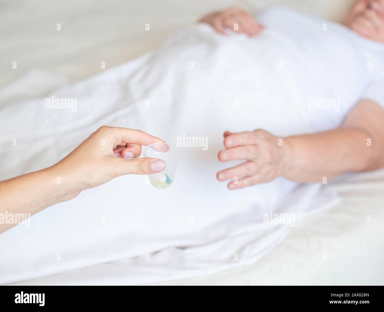 The doctor holds out an elderly woman a pill for dizziness. Woman lying on bed, concept of treating illness with pills Stock Photo