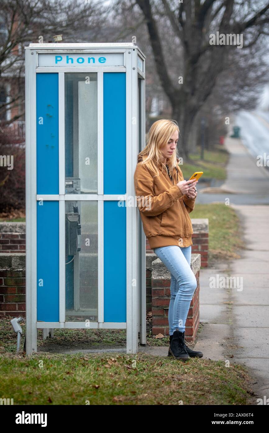 A woman leaning on a phone booth checks her smart phone , Lancaster, Pennsylvania, USA Stock Photo