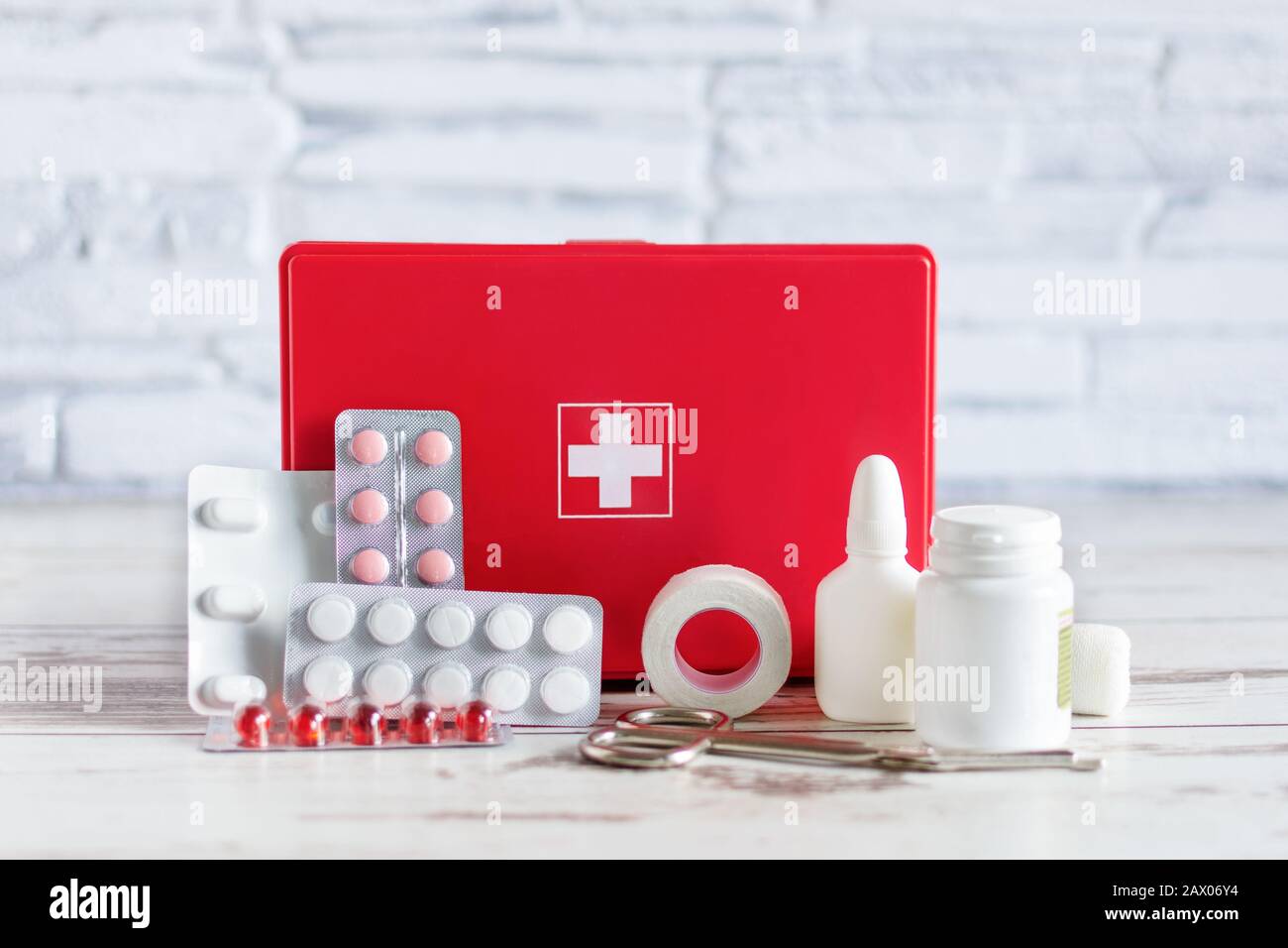 First aid kit red box with medical equipment and medications for emergency on white wooden background over brick wall. Stock Photo