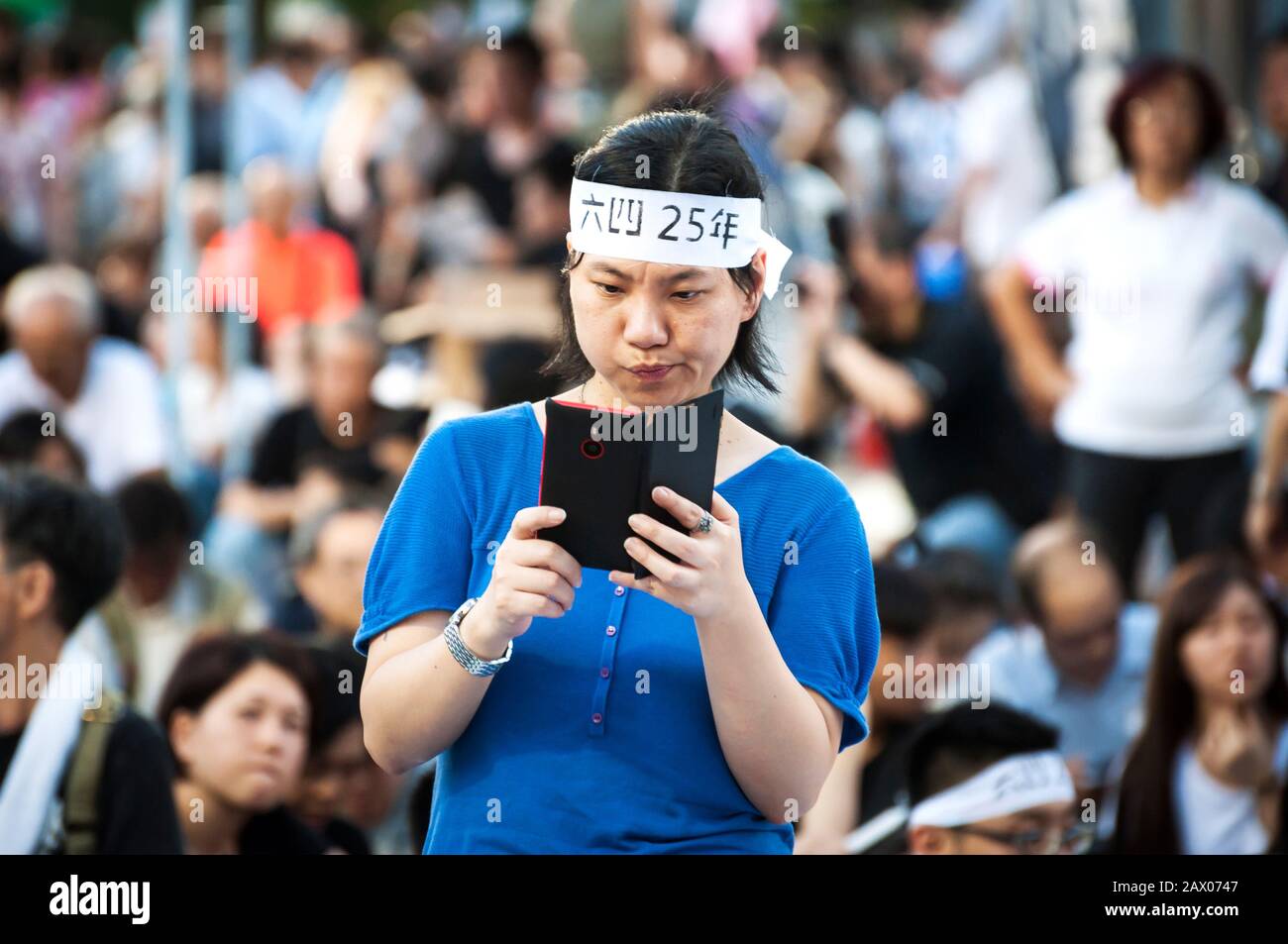 Woman wearing a headband takes a photo at the 25th anniversary commemoration of the Tiananmen Square masacre in Victoria Park, Hong Kong Stock Photo