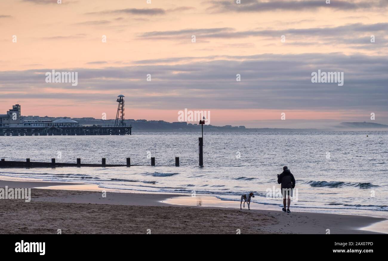 Man and dog taking an early morning walk at dawn by the sea at Bournemouth Stock Photo