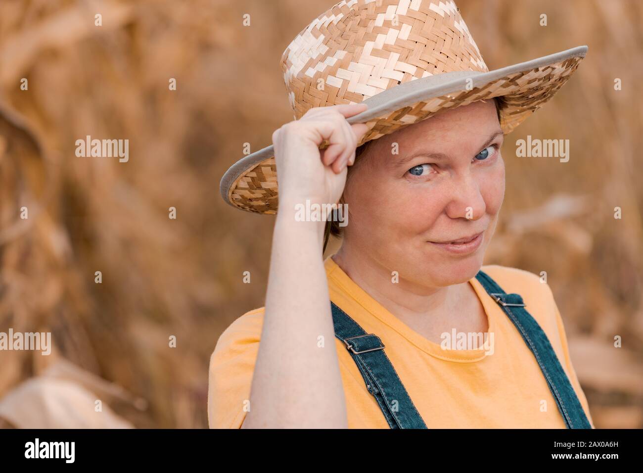 Portrait of female corn farmer in field wearing straw hat and bib ...