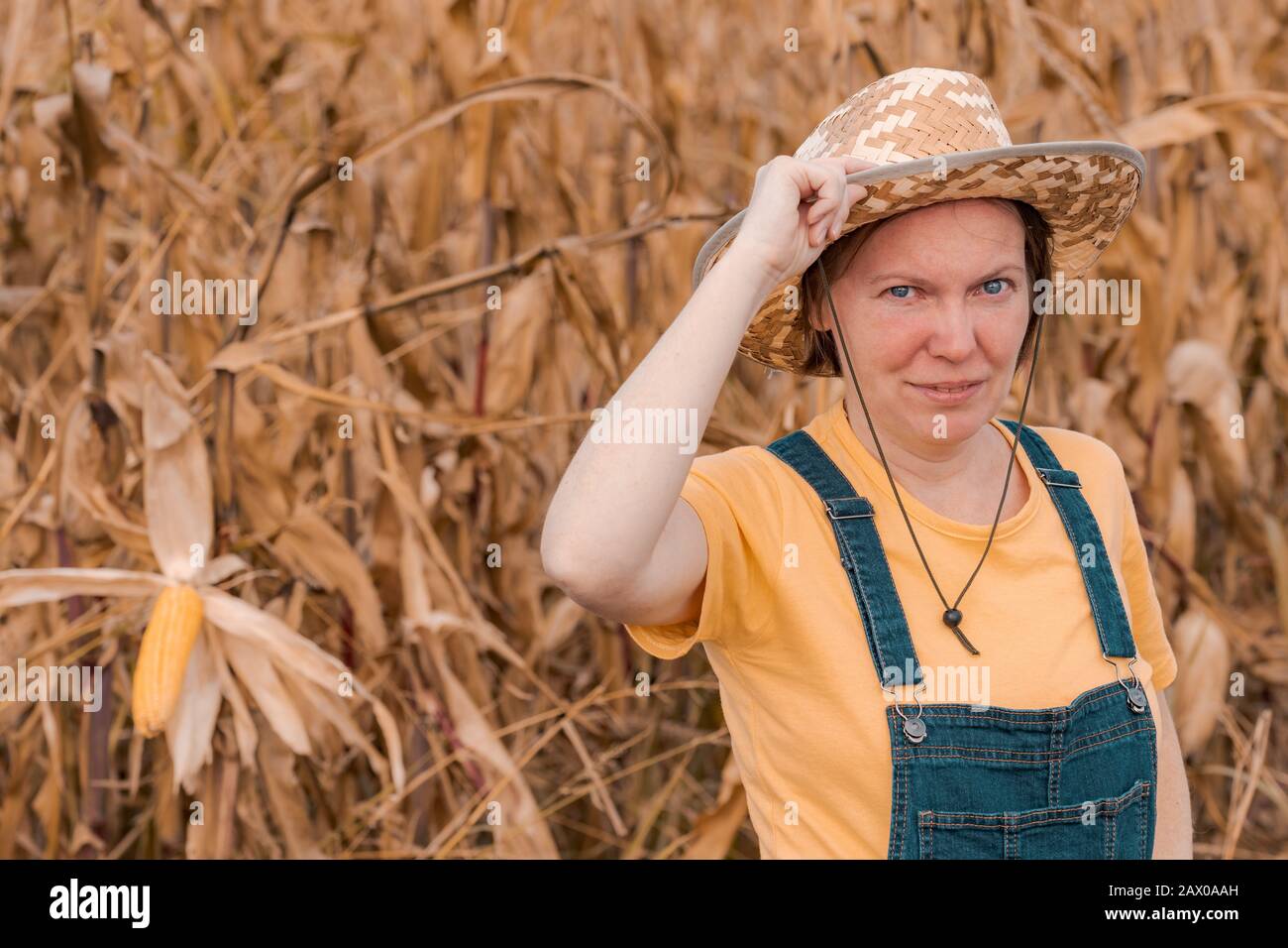 Portrait of female corn farmer in field wearing straw hat and bib ...