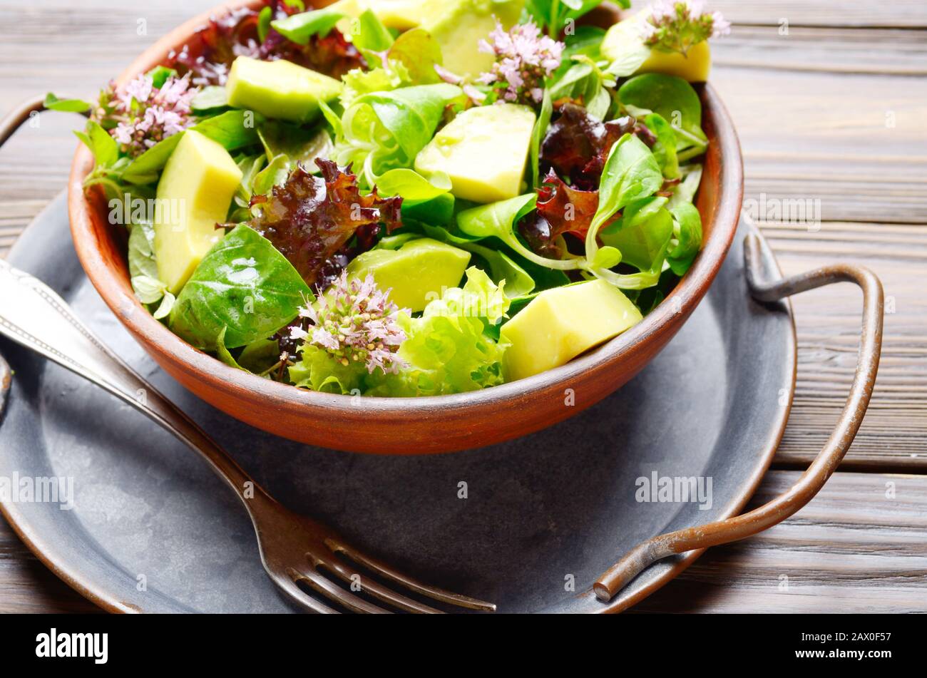 Clay dish with salad of avocado, green and violet lettuce, lamb's lettuce and oregano flowers with vintage fork aside Stock Photo