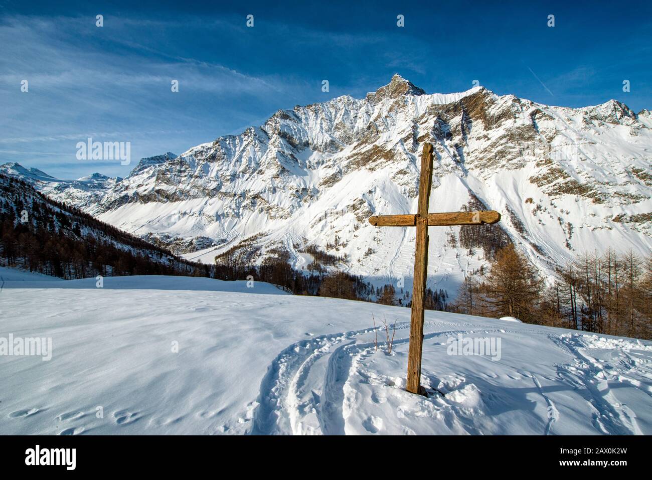 Italy valle d'Aosta Val di Rhemes - The cross at Plan de la Feye, where you exit the woods to go up to the pastures of the Entrelor. From here it is possible to have an overall view of the upper Val di Rhemes. In the background, the Grande Rousse massif. Stock Photo