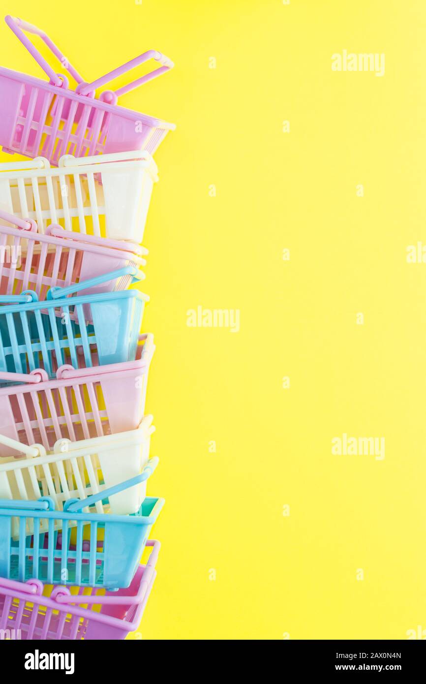 Pile of colourful plastic shopping baskets on a yellow background. Vertical orientation Stock Photo