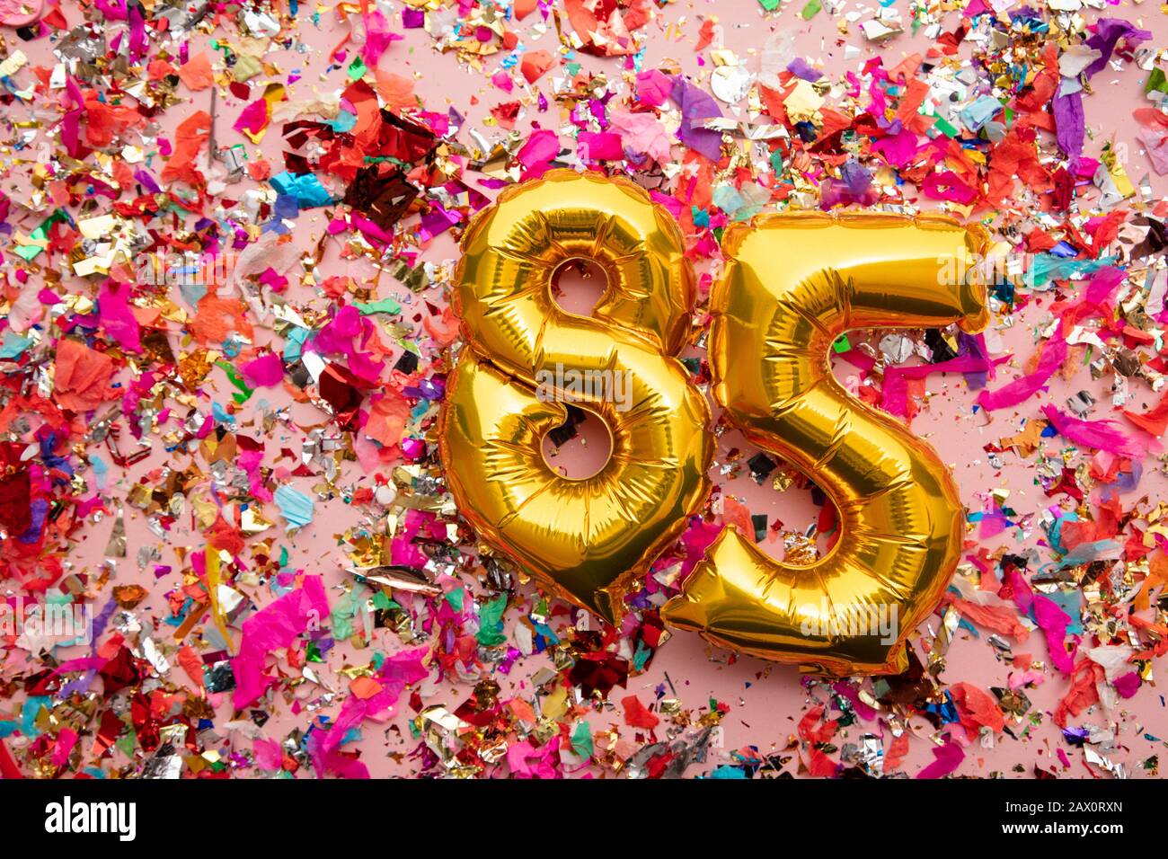 Number 85 gold birthday celebration balloon on a confetti glitter background Stock Photo