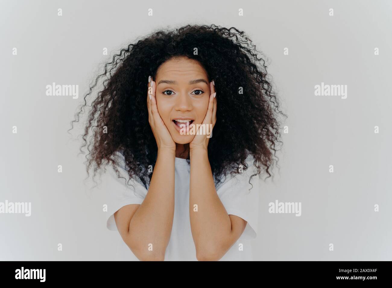 Photo of surprised cheerful woman with Afro haircut, keeps both hands ...