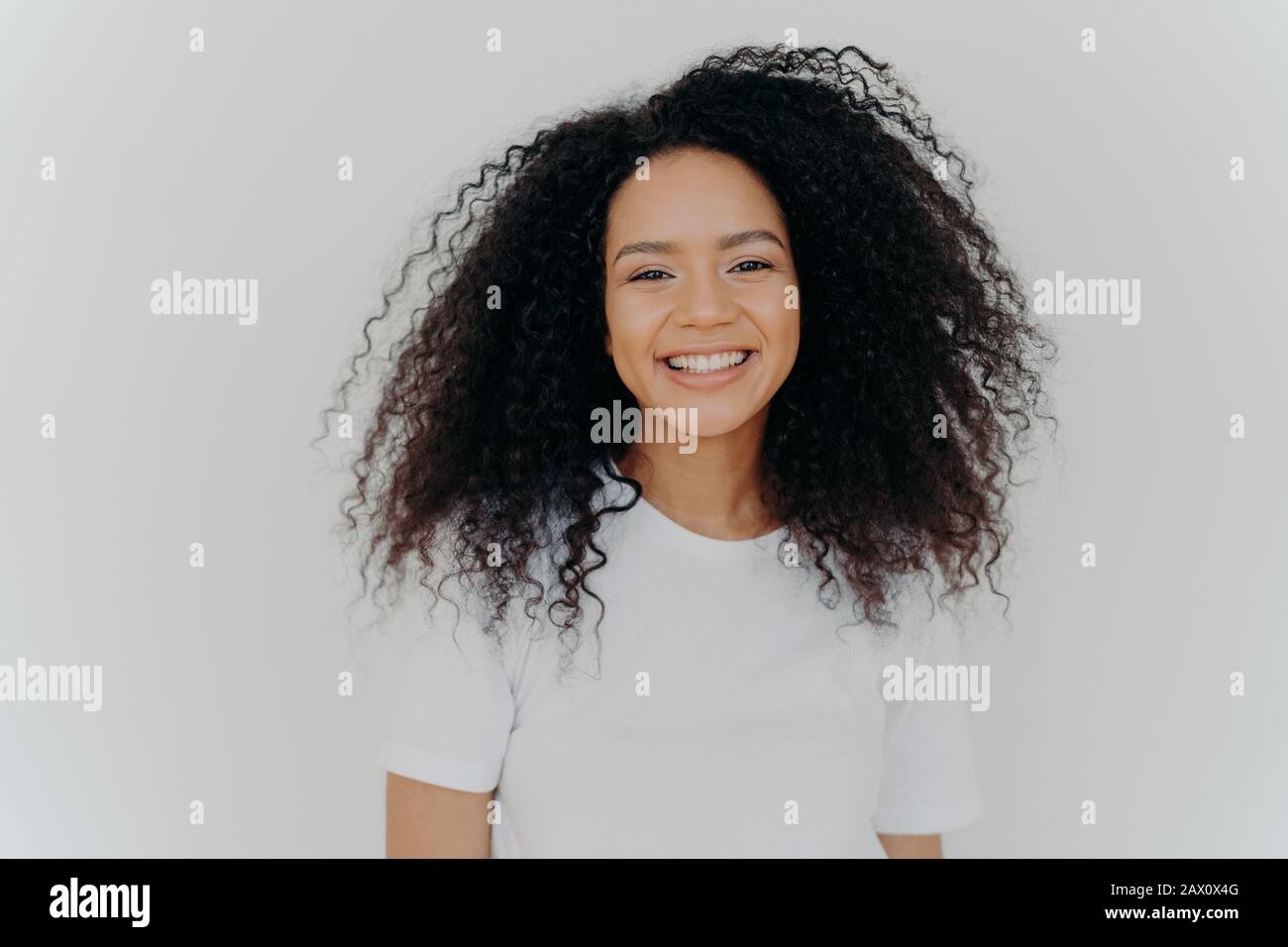 Pleasant looking young woman has toothy smile, happy face expression, laughs at something funny, shows white perfect teeth, dressed casually, isolated Stock Photo