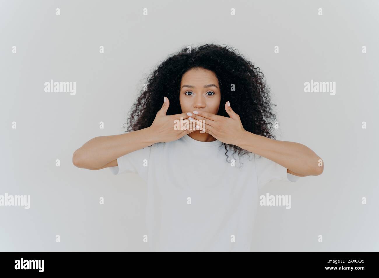 Horizontal Shot Of Surpised Dark Skinned Woman Covers Mouth With Both 