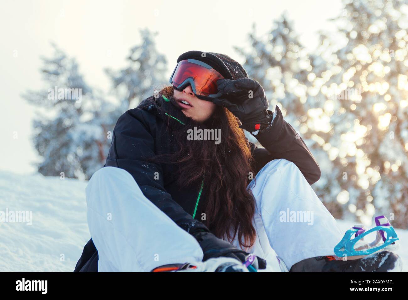 Stock photo of a young girl snowboarder who is sitting on the snow of the mountain Stock Photo