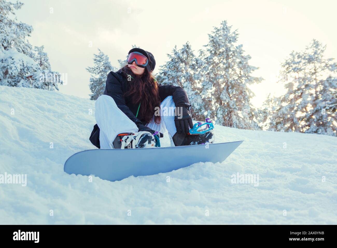 Stock photo of a young girl snowboarder who is sitting on the snow of the mountain Stock Photo