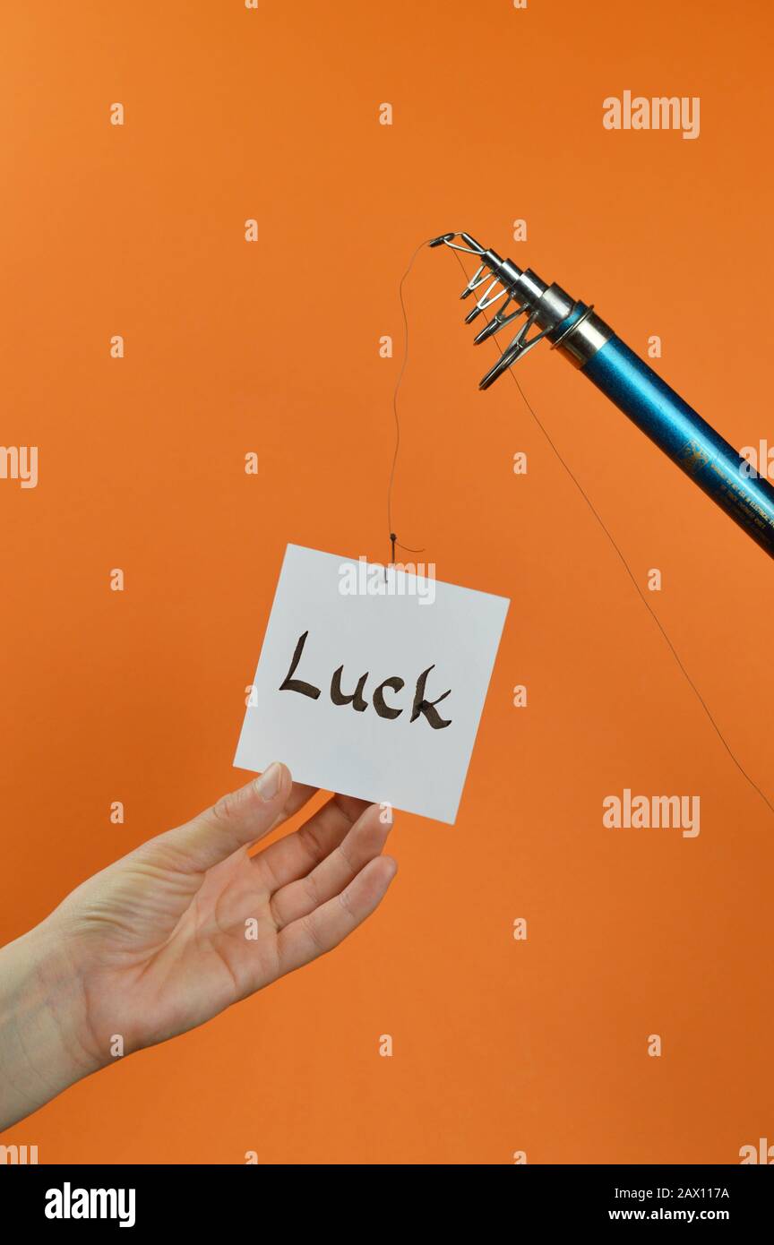 a hand grabbing for a piece of paper with the word LUCK on it hanging from a fishing line Stock Photo
