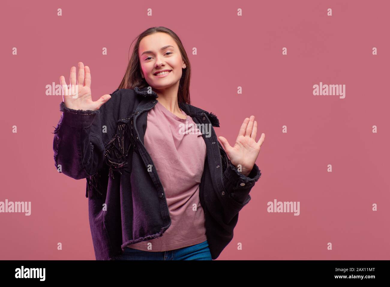 Young brunette woman on pink background. High five, informal style of clothing, jeans and a cowboy shirt with fringe. Stock Photo