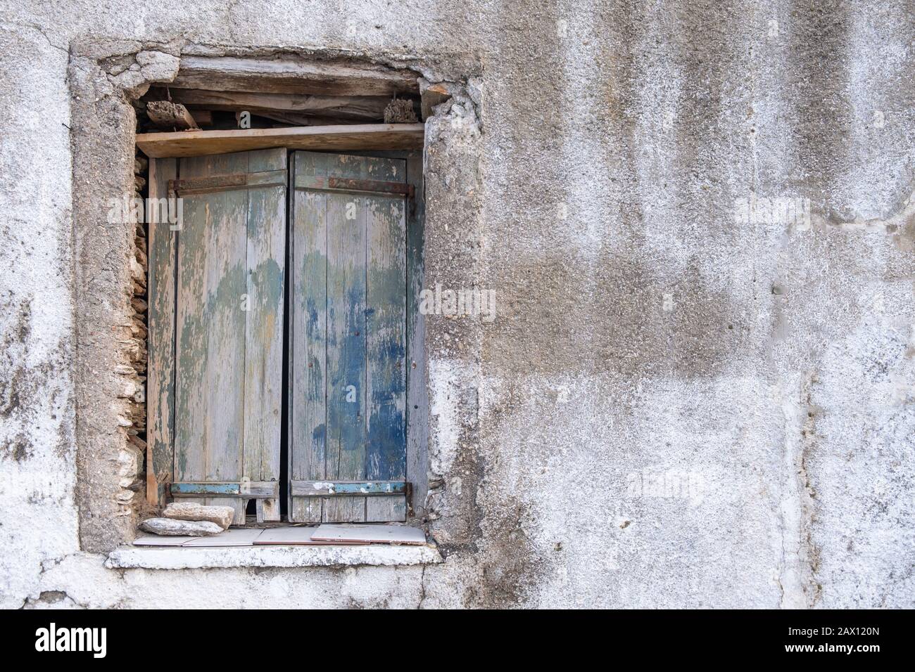 Old double closed wooden shutters. Rusty hinges on peeled planks,  stones keep the window shut. Wall empty and faded. Copy space. Stock Photo
