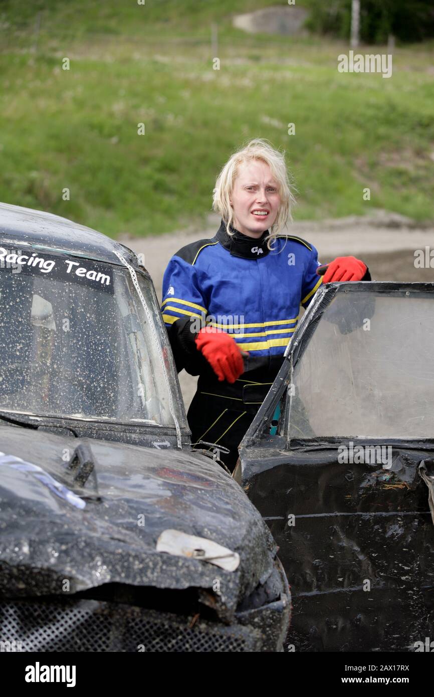 Young feminine driver next to her battered BMW in Swedish Folkrace is as tough as they come.  Torslanda. Sweden. Stock Photo