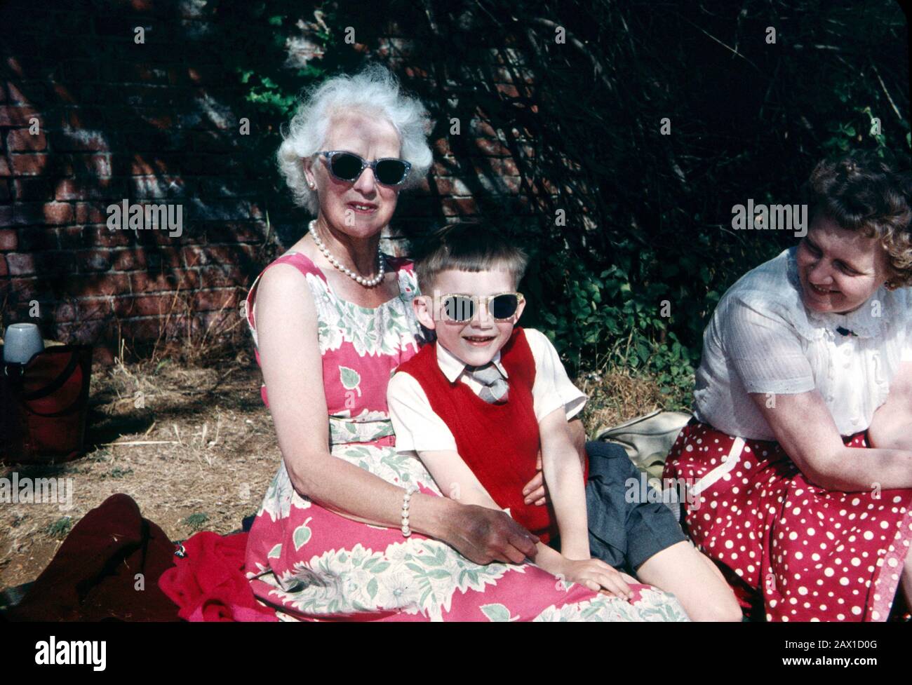 Six year old boy wearing dark glasses sitting having a picnic with older relatives in 1959 Stock Photo