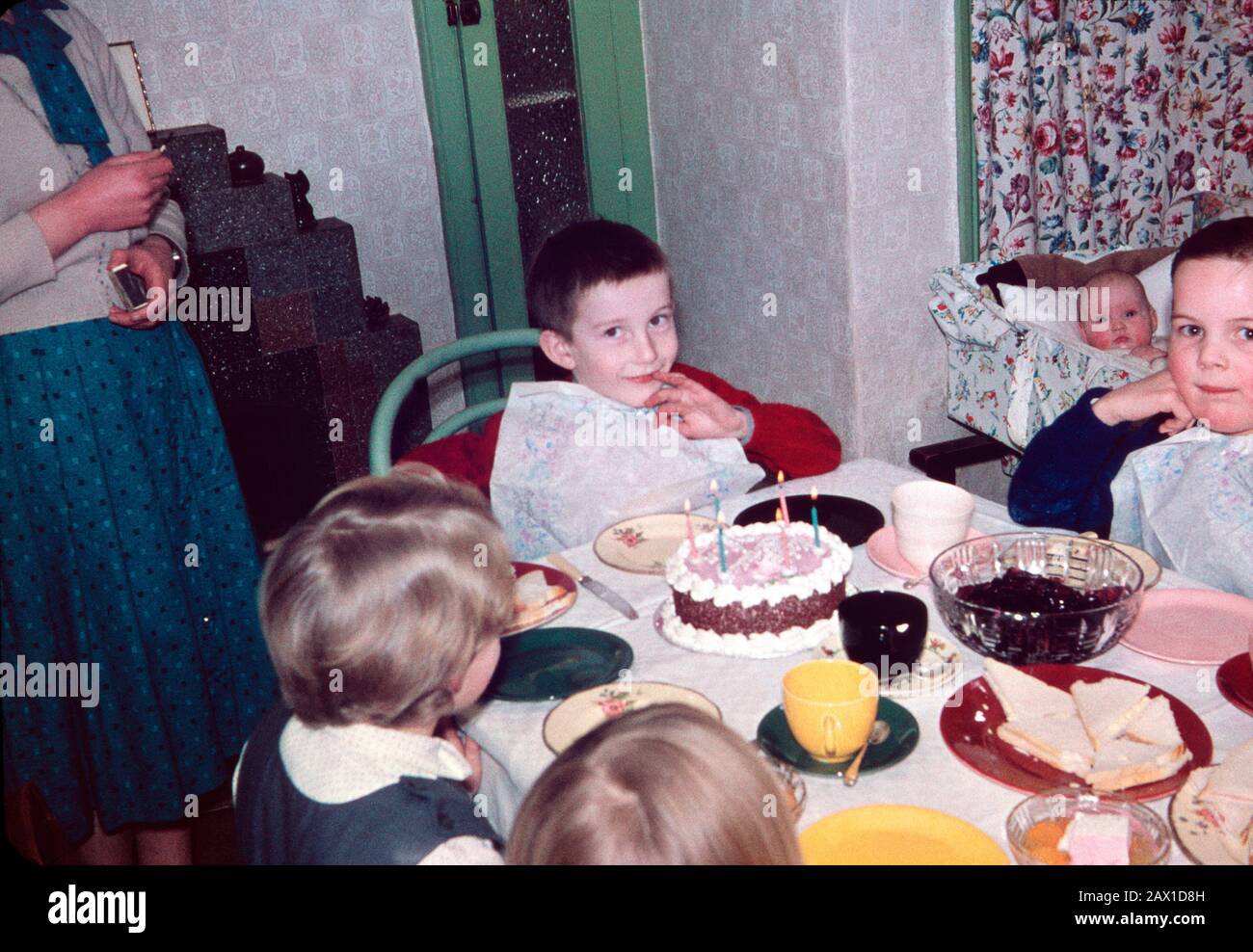 Six year old Ian Pilbeam at his birthday party with sister in cot and mother having lit the candles, February 1960 Stock Photo