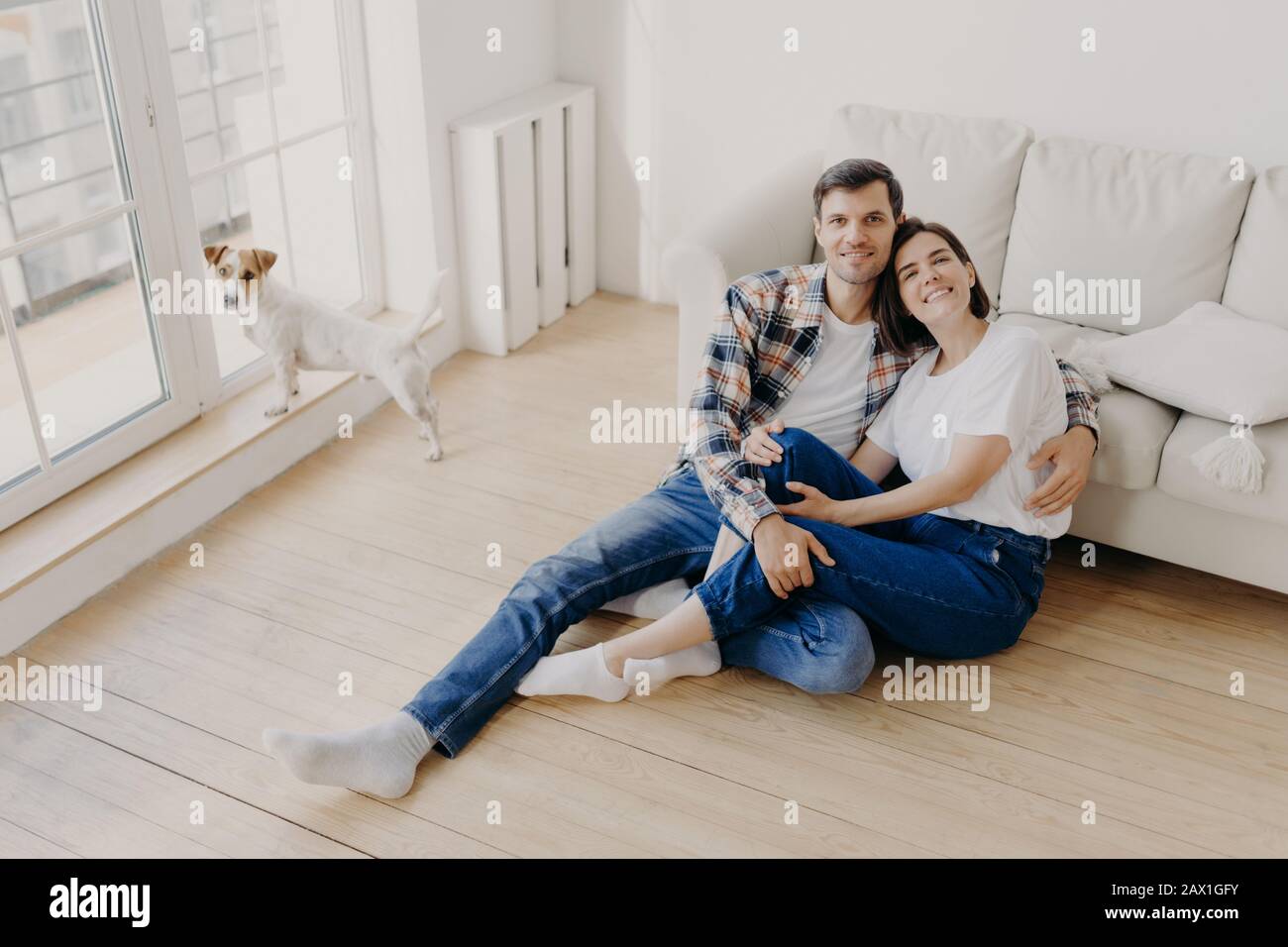 Romantic couple enjoy togetherness, embrace and feel support of each other, sit on floor near sofa, glad to spend free time together, dressed casually Stock Photo