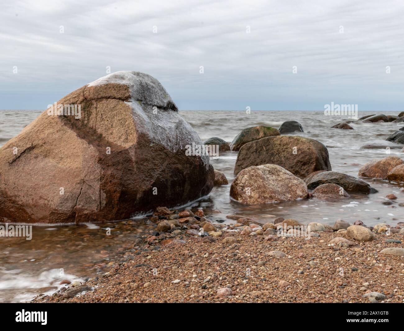 landscape with rocky beach in the evening, sun hiding behind clouds, beautiful sky Stock Photo