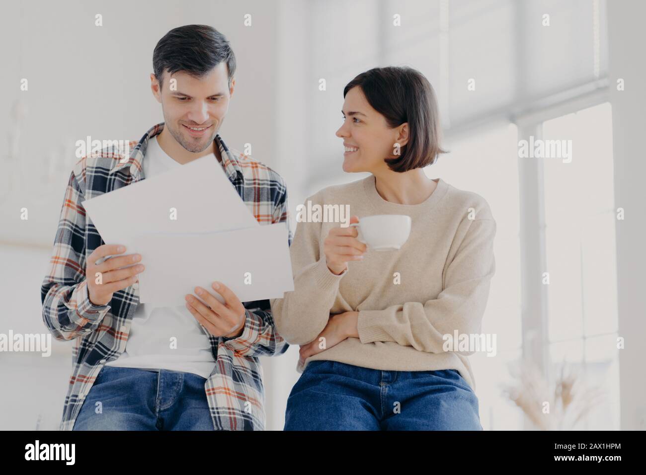 People, finances and collaboation concept. Happy European family couple analyze documents or contract terms, work with documentation, woman drinks cof Stock Photo