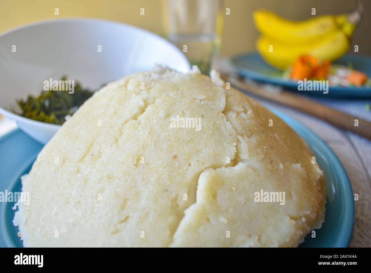 heap of ugali on a plate with sukuma and fruits in the background Stock Photo