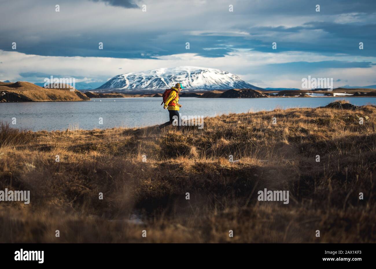 Woman walking through field next to lake with mountains in distance Stock Photo