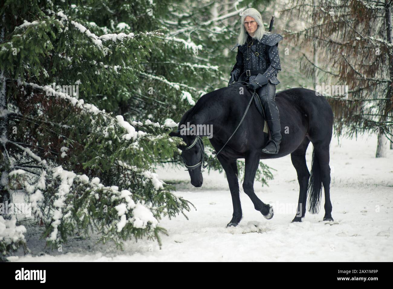 Man in image of ancient warrior witcher riding a horse in snow winter forest. Stock Photo
