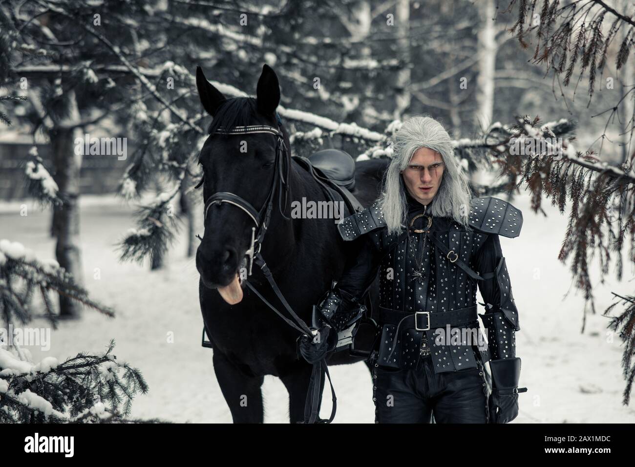 Man in image of ancient warrior witcher next to a horse in snow winter forest. Stock Photo