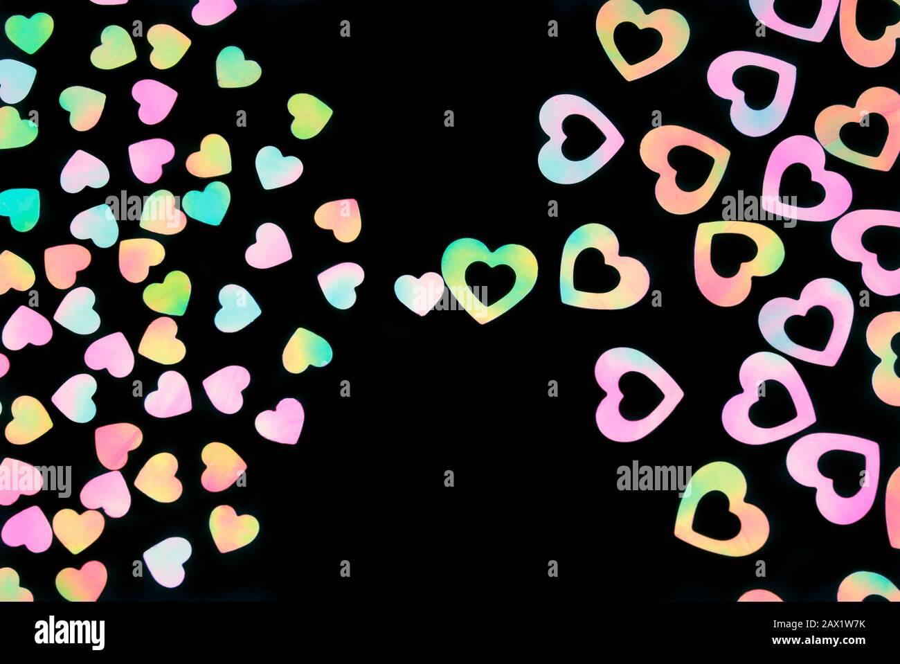 Colorful iridescent hearts attracting together in the center of a black background Stock Photo