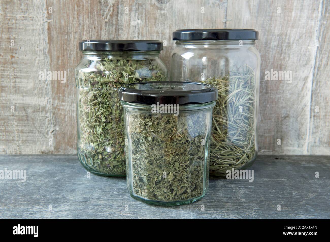 Old jars with black lids reused to store organic dried herbs against wooden background. Herb jars.  Zero waste concept. Stock Photo