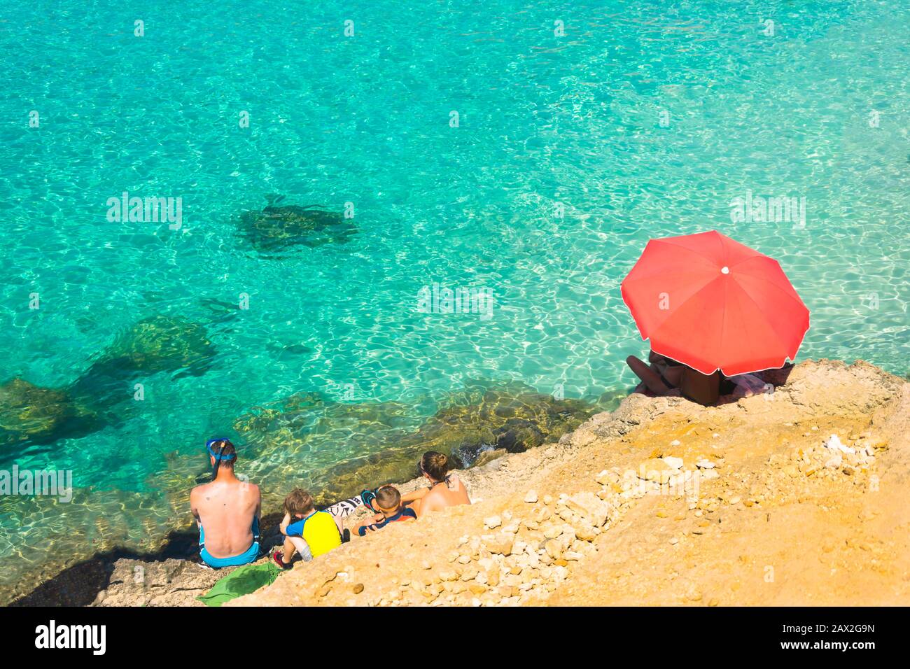 Comino Blue lagoon beach tourists and azure Malta sea. Aerial beach scene with red parasol in summer holiday season. Malta vacation turquoise sea. Stock Photo