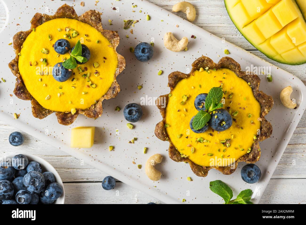 Vegan raw mango cheesecakes with fresh berries, mint and nuts. healthy vegan gluten free food concept. top view Stock Photo