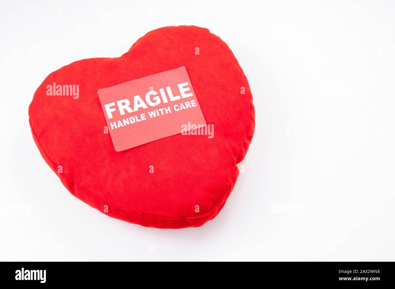 Valentine's Day heart cushion sitting on white background with a Fragile Handle With Care Sticker Stock Photo