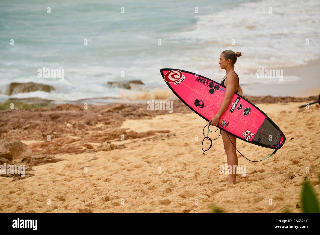 Female surfer holding pink surfboard on beach after riding massive