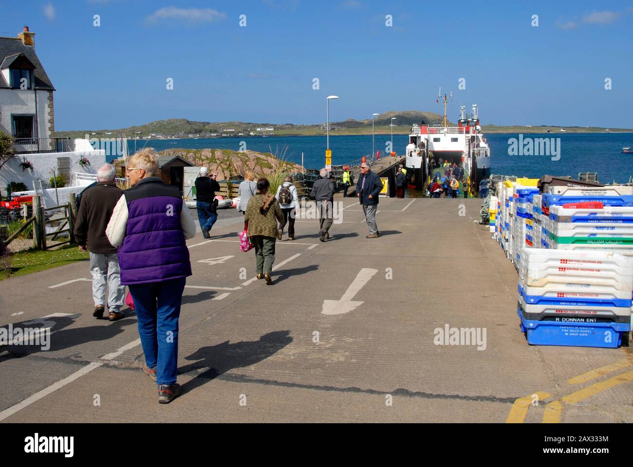 Passengers joining and disembarking a ferry, Mull, for the short sea crossing to the Island of Iona, Scotland with the Abbey visible in the distance Stock Photo