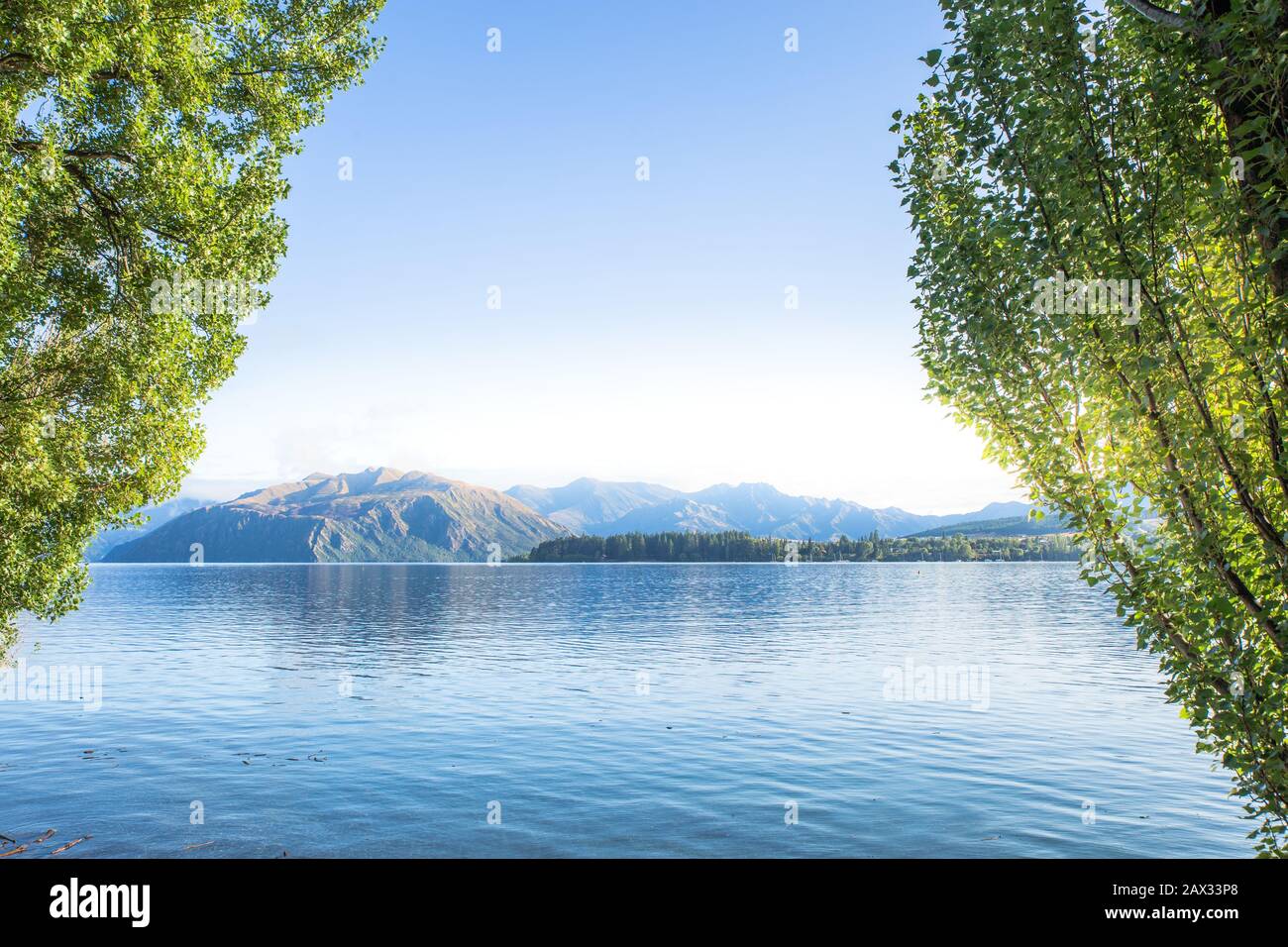 Early morning lake sunrise with golden light. Blue sky and water. Lake Wanaka New Zealand, Popular travel destination. Stock Photo