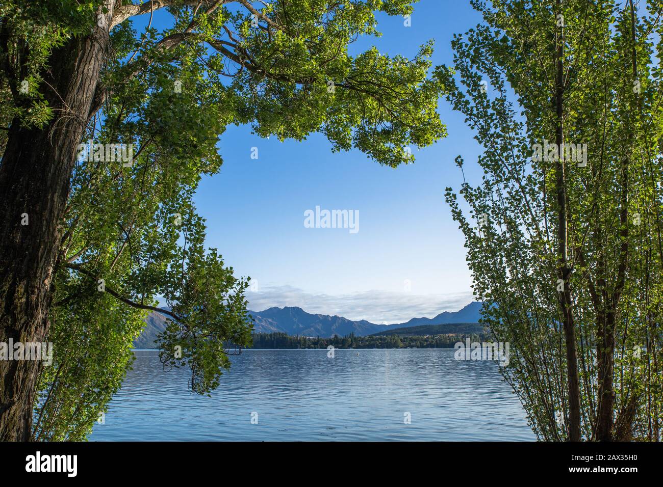 Early morning lake sunrise with golden light. Blue sky and water. Lake Wanaka New Zealand, Popular travel destination. Stock Photo