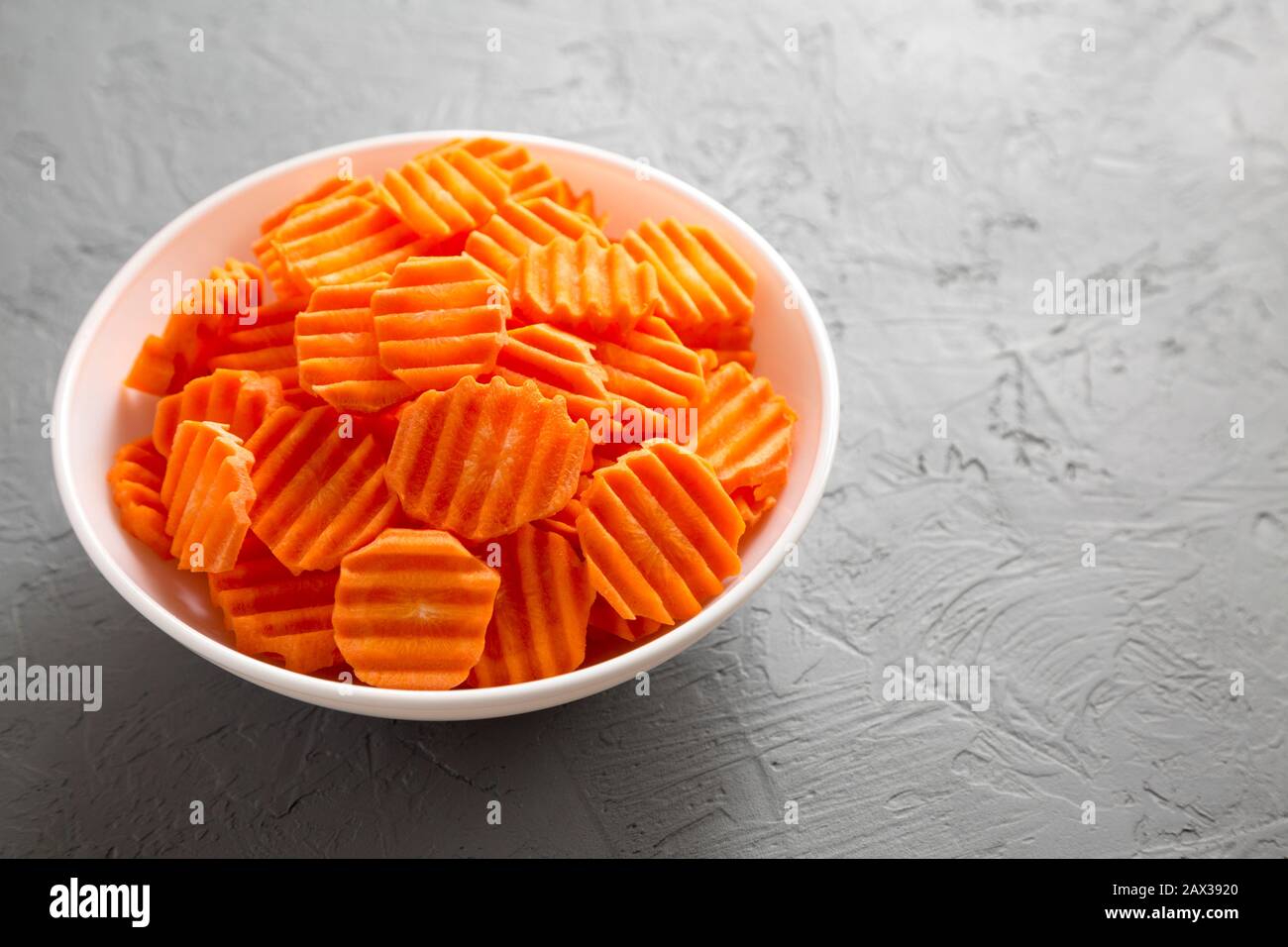 Fresh Raw Organic Carrot Chips in a bowl over gray background, low angle view. Copy space. Stock Photo
