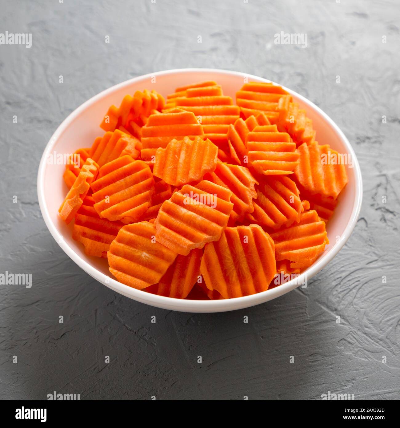 Fresh Raw Organic Carrot Chips in a bowl over gray surface, low angle view. Close-up. Stock Photo
