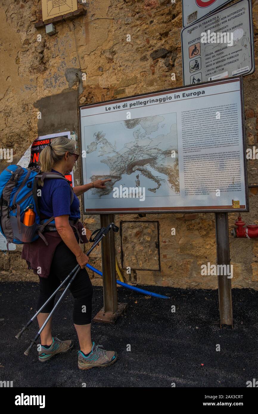 Woman backbacker hiker with racksack on the pilgrimage route Via Francigena looking at a large map at Abbadia Isola monastery Monteriggioni, Tuscany Stock Photo