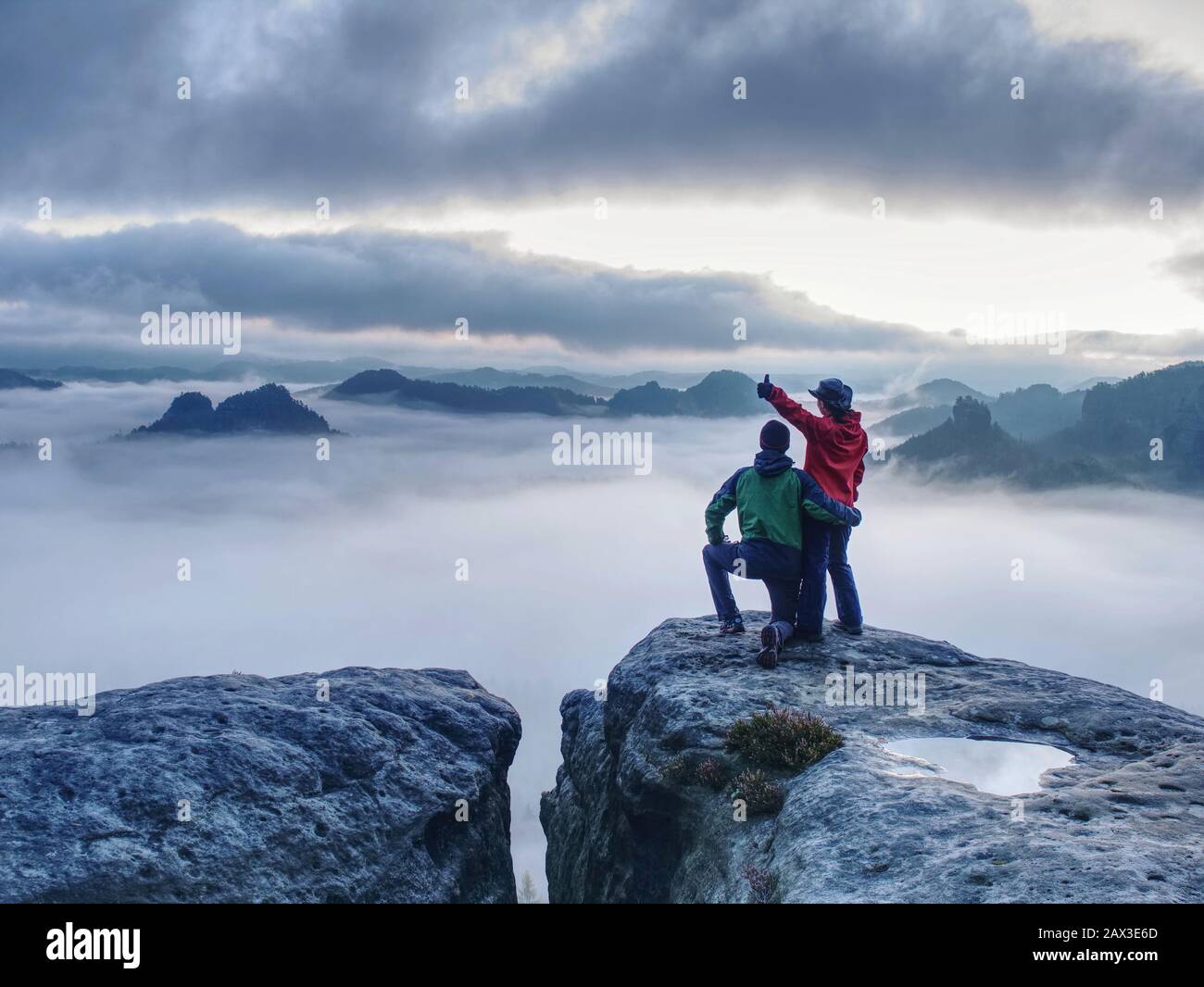 Lovely heterosexual Couple looking at far sunrise in heavy clouds. The dark night in foggy mountains ends. Stock Photo