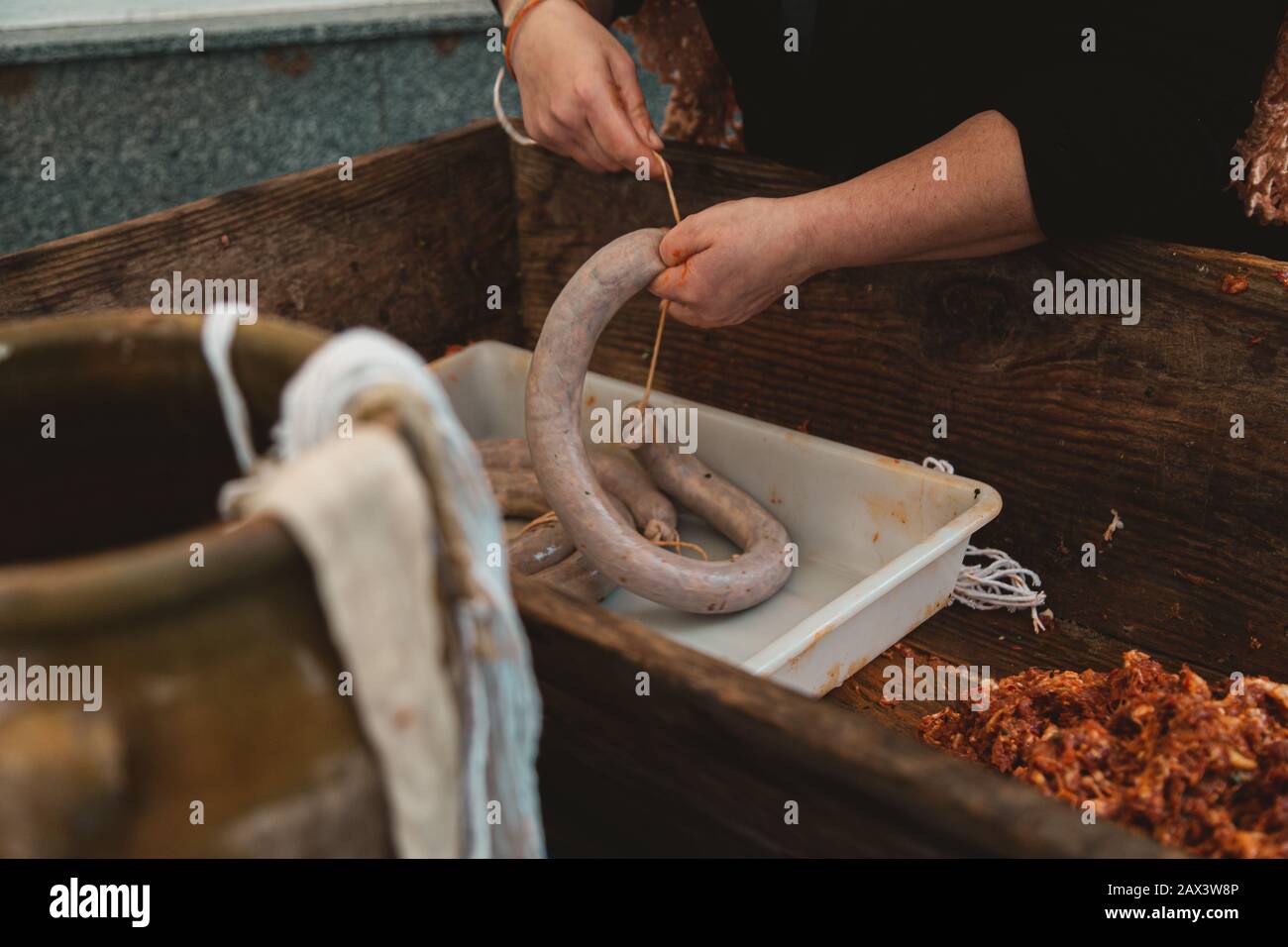 Closeup of a person preparing a raw kielbasa in a wooden pot under the lights Stock Photo