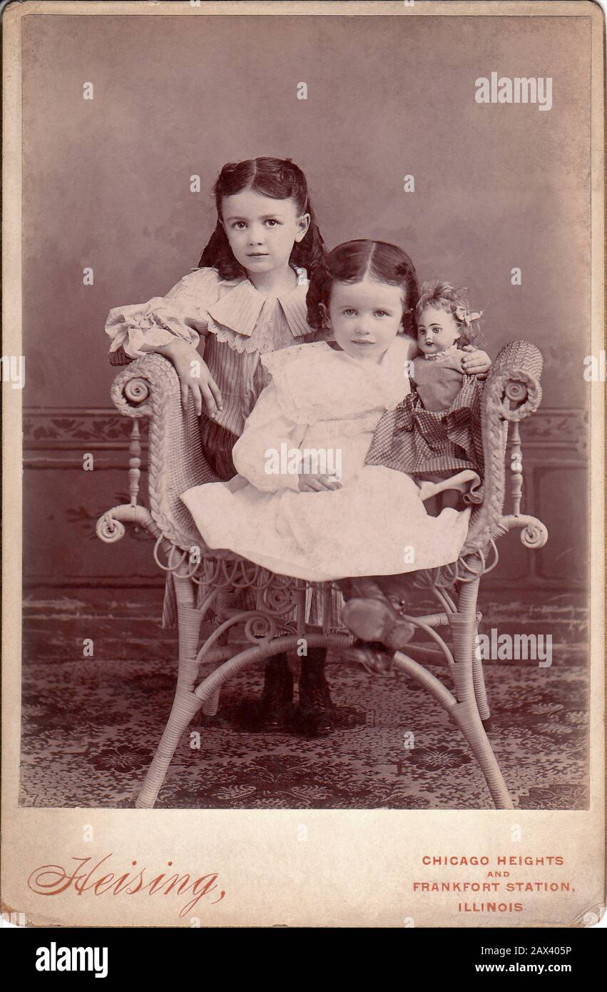 1895 ca, CHICAGO , USA : Little girls with doll . Photo by Heising , Chicago , Illinois  - FOTO STORICHE - HISTORY PHOTOS -  BAMBINA -  CHILD - BAMBINO - BAMBINI - BAMBINE - CHILDREN -  tenerezza - tenderly - CHILDREN - BAMBINA - BABY - OTTOCENTO - BELLE EPOQUE - FASHION - MODA INFANTILE - BABY -  bebé  - pink dress - CHILDHOOD - INFANZIA - bambola - bambole - toys - giocattolo - giocattoli - gioco - play - poltrona di vimini - rattan - pizzo - lace - sorella - sorelle - sisters  ----- Archivio GBB Stock Photo